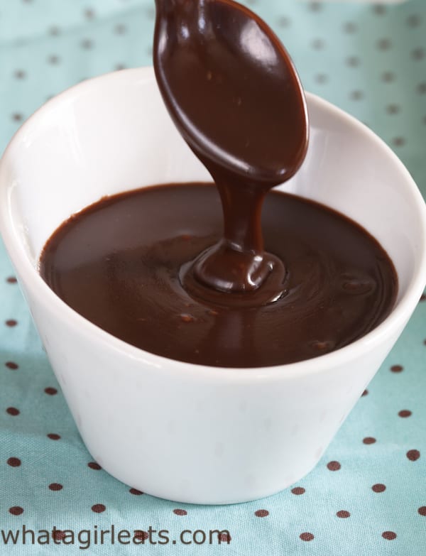 Spoonful of bittersweet chocolate sauce drizzling into in a white bowl filled with chocolate sauce.