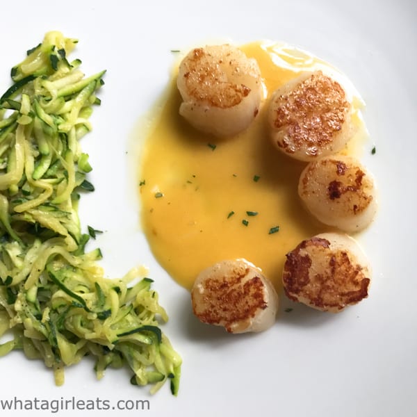  Scallops on a plate wit saffron beurre blanc and zucchini noodles on the side.