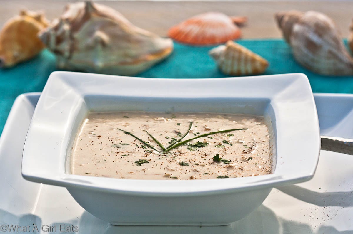 She Crab Soup in a square white bowl with a blue napkin and seashells in the background.