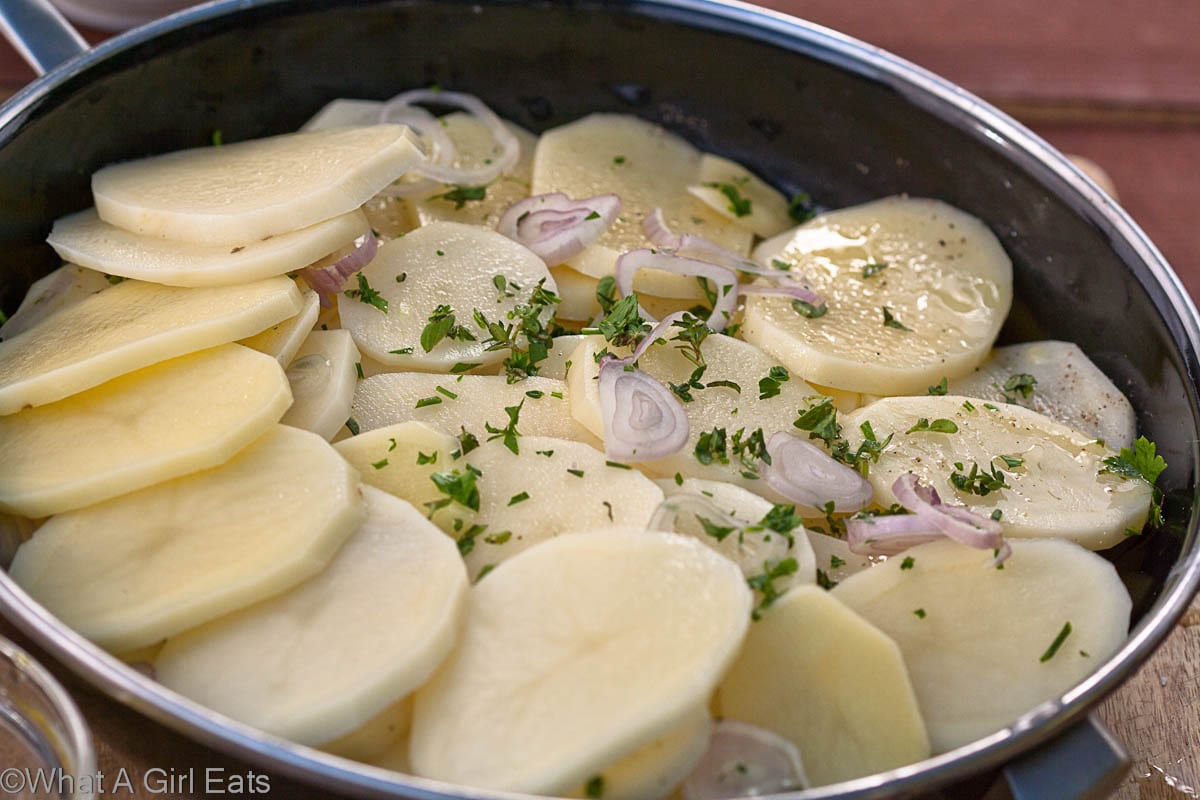 Potatoes in a pot, arranged in a circle with herbs, shallots, butter and seasoning.
