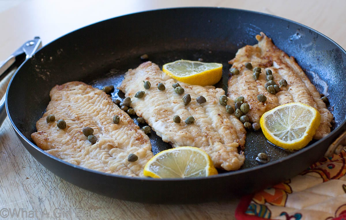 Sole cooking in a cast iron skillet with capers and lemon slices.