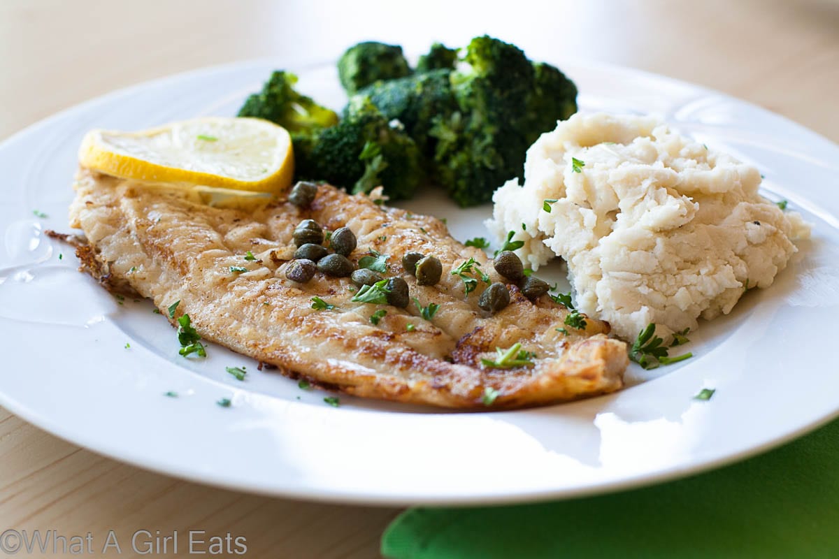 Dover Sole on a white plate with mashed potatoes and broccoli.