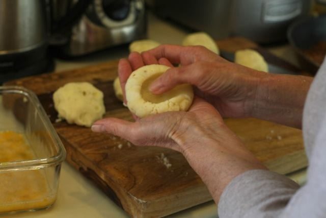 Hands forming indentation in potato balls.
