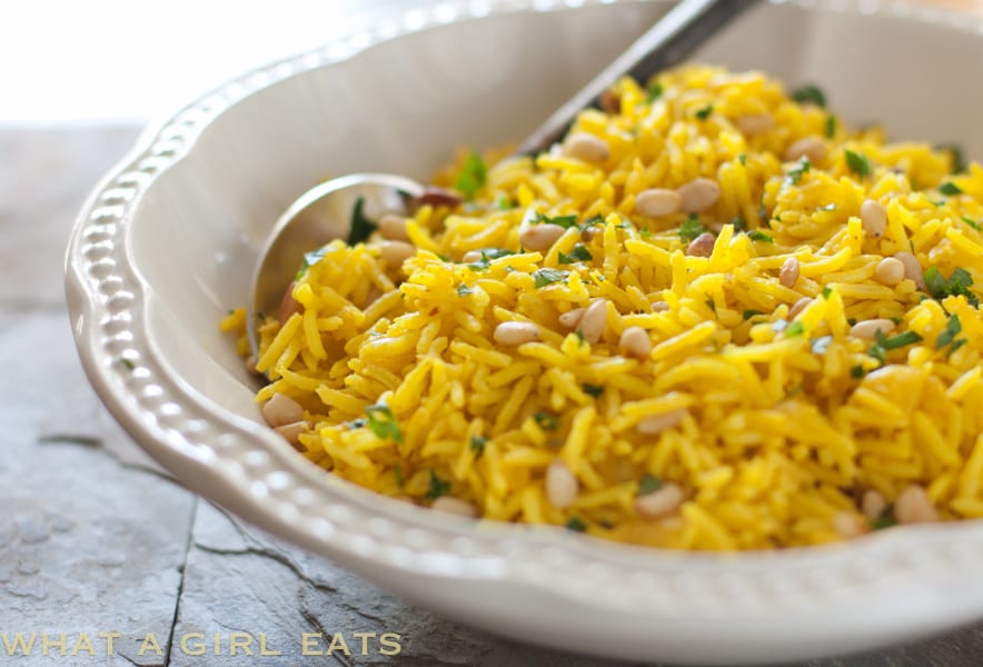 Golden Mediterranean Rice Pilaf in a white bowl with a spoon in it.