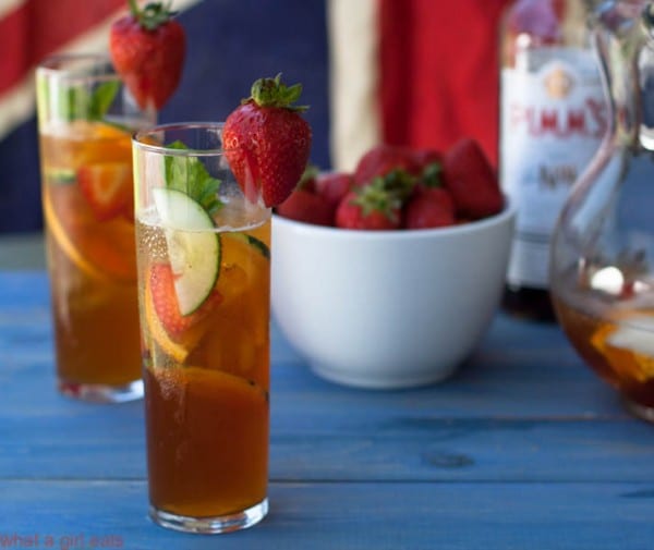 Two tall glasses of Pimm's Cup with a bowl of strawberries and bottle of liquor in the background.