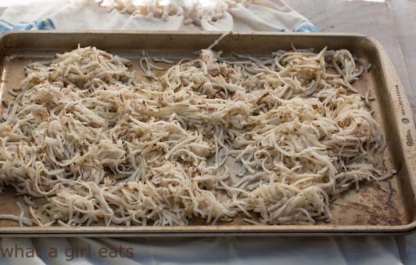 Shredded potatoes being dried out on a baking sheet.