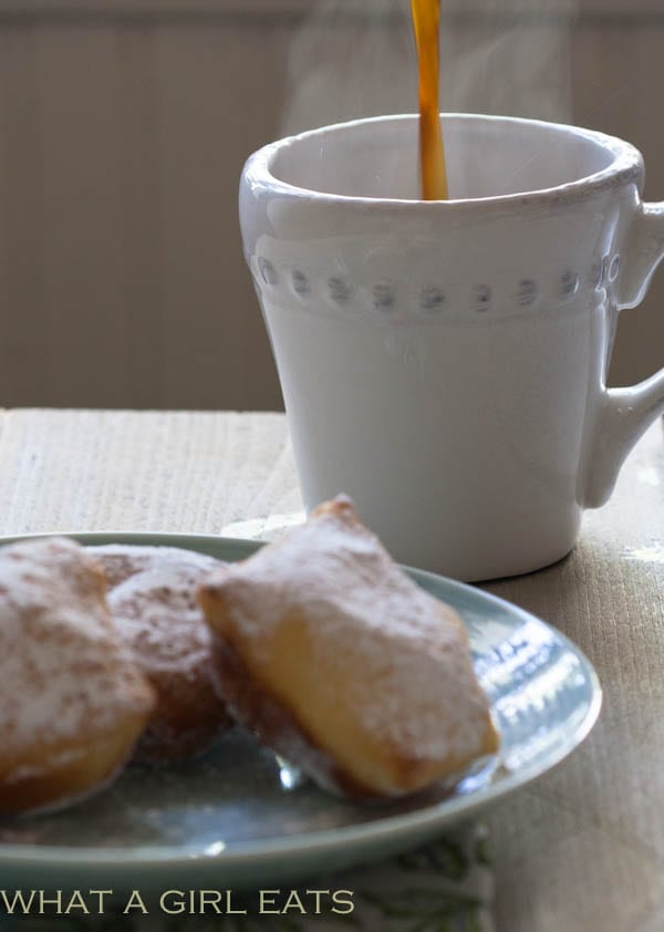 Cup of coffee and beignets on a plate.