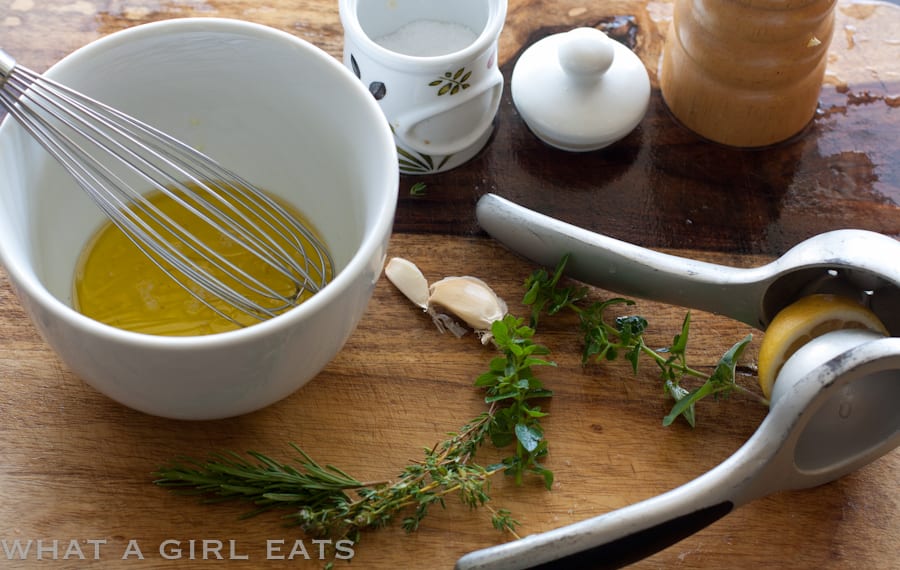Lemon marinade in a bowl with a whisk and herbs.