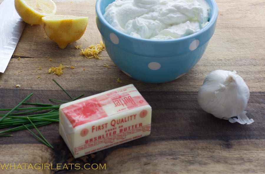 Yogurt, butter, garlic, chives, and lemon on a table.