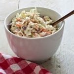 Creamy cole slaw on white picnic table with red and white cloth.