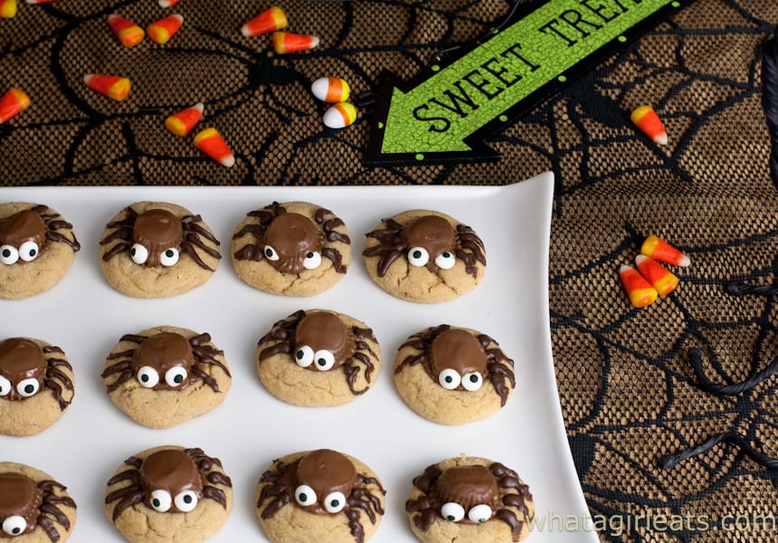Peanut Butter Cup Spider Cookies on a white plate with candy corn scattered on the table nearby.