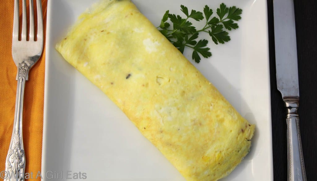 Perfect French omelette on a white plate with a fork and knife next to it.