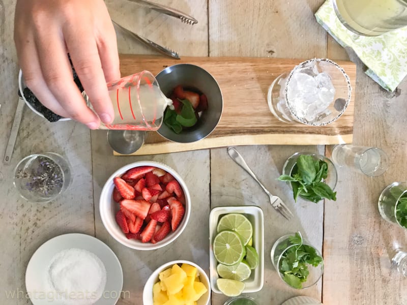 Hand pouring lime juice into a cocktail shaker with strawberries and basil for Strawberry-Basil Margarita.