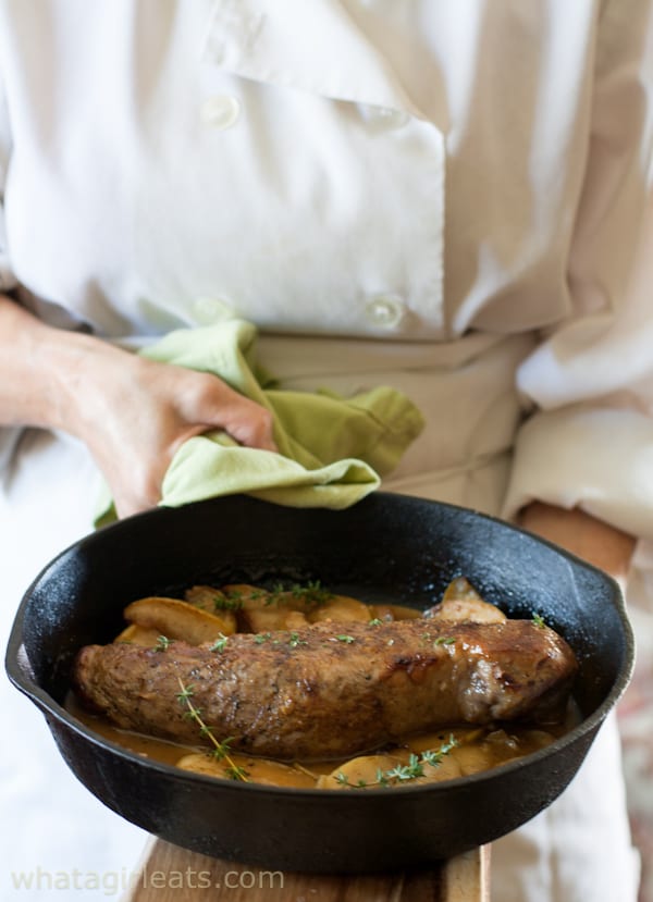 Chef holding a skillet with pork tenderloin with apples.