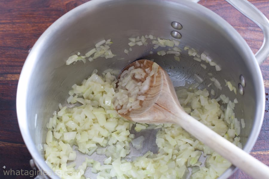Sauteed onions in a pan with a wooden spoon.