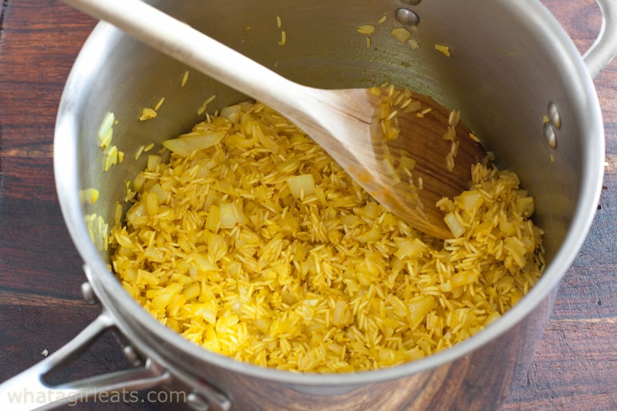 Uncooked rice pilaf being mixed in a pan with a wooden spoon.