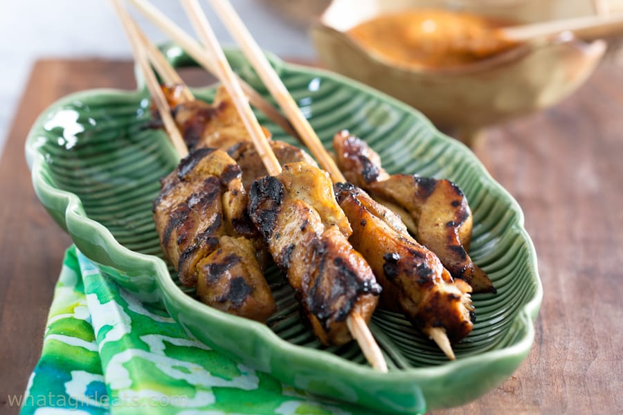 Thai satay chicken on skewers on a green, leaf-shaped platter.