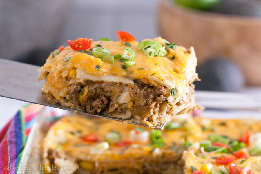 A slice of layered enchilada casserole being lifted out of the pan.