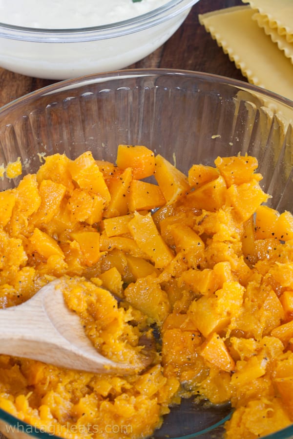 Mashing butternut squash in a bowl with a wooden spoon.