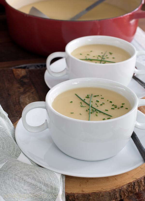 Two white cups of potato leek soup with chives garnish on top.