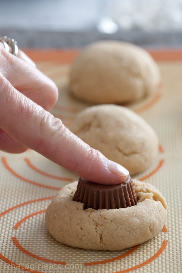 Finger pushing peanut butter cup into the cookie.