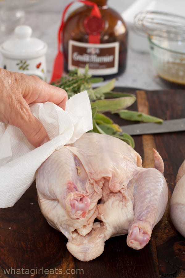 Patting the cornish hen dry with a paper towel.