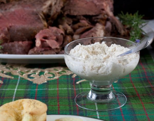 Horseradish sauce in glass bowl next to prime rib on a platter.