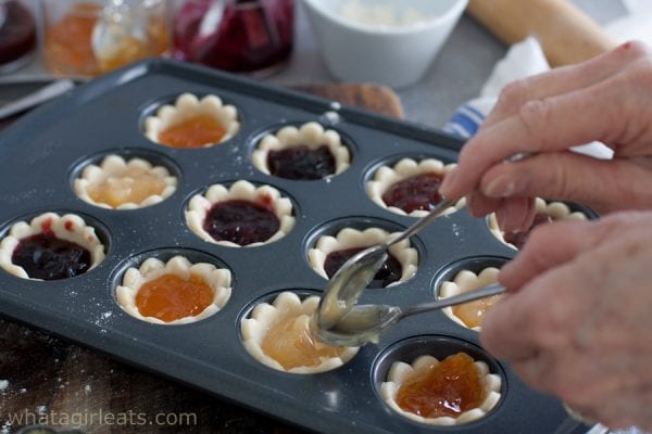 Spooning jam into raw dough tart shells.