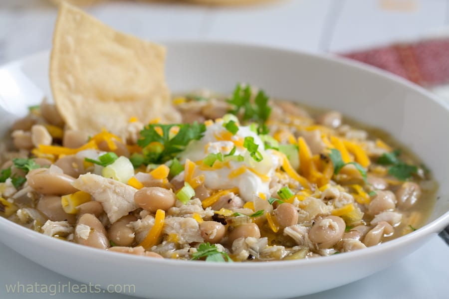 White chicken chili in a bowl topped with sour cream, cheese, and green onions.