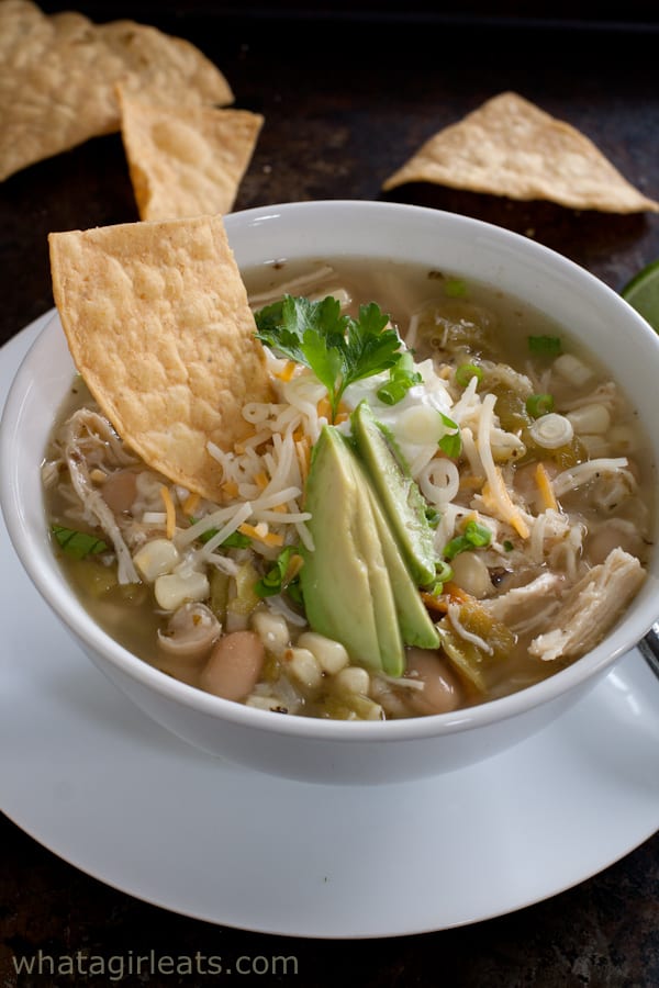 White chicken chili in a bowl, topped with avocado and a tortilla chip.