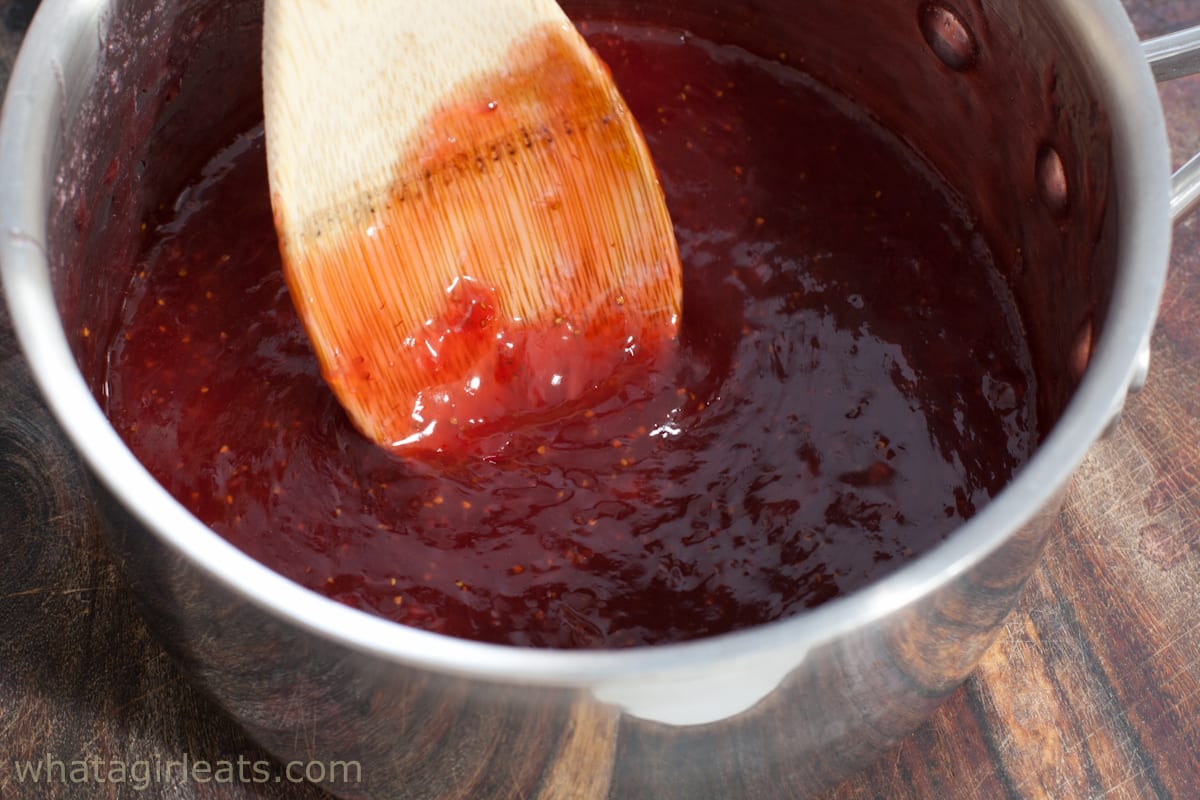 Strawberry glaze in pan with a wooden spoon.