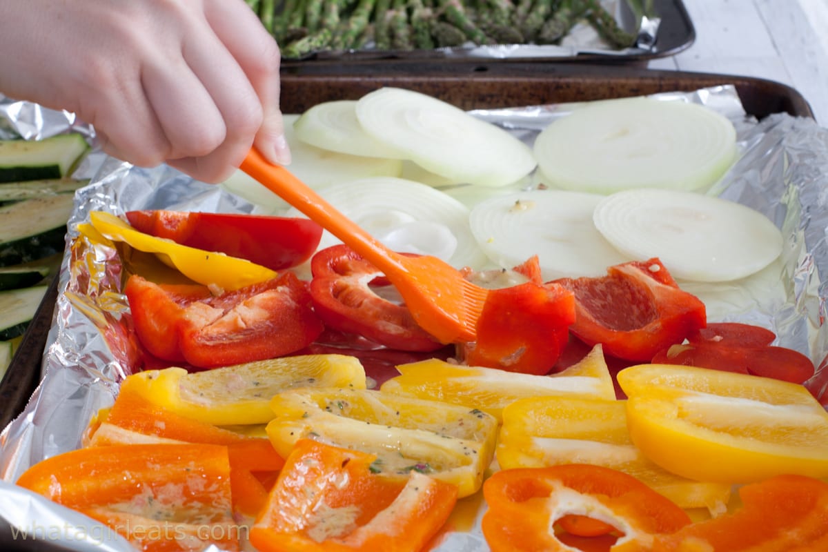 Brushing vegetables with marinade on a baking sheet.