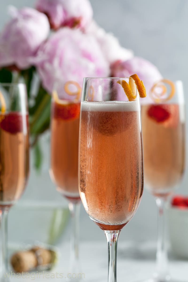Closeup of kir royale cocktail with orange peel and raspberry garnish.
