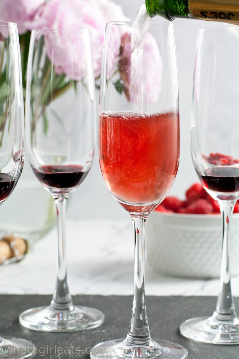 Creme de cassis in champagne glasses with champagne being poured into one glass. 