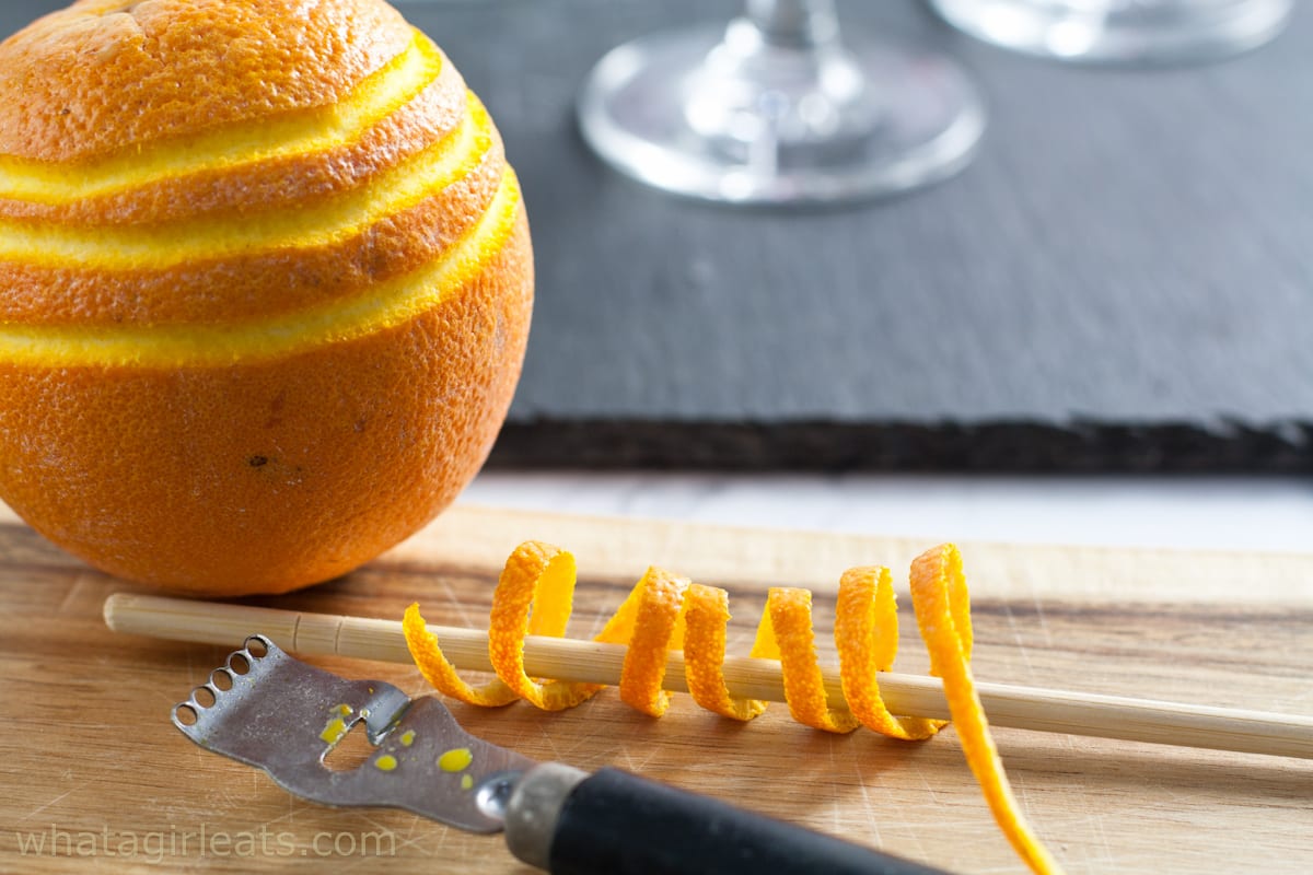 Channel knife next to an orange with  peel wrapped around a wooden skewer.