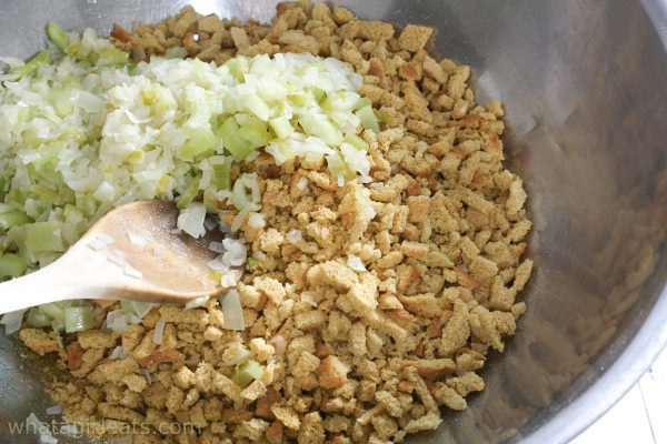 Bread, onions and celery in a large bowl with a wooden spoon.