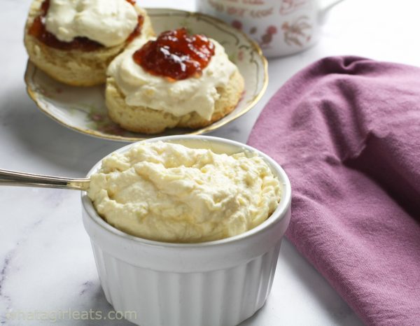 Cream in white ramekin with scones in background.