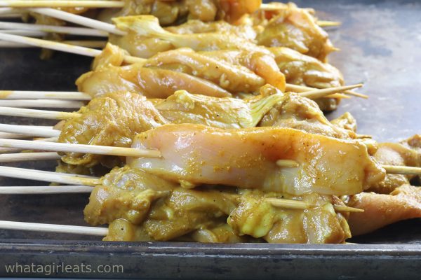 threading chicken on bamboo skewers for satay.
