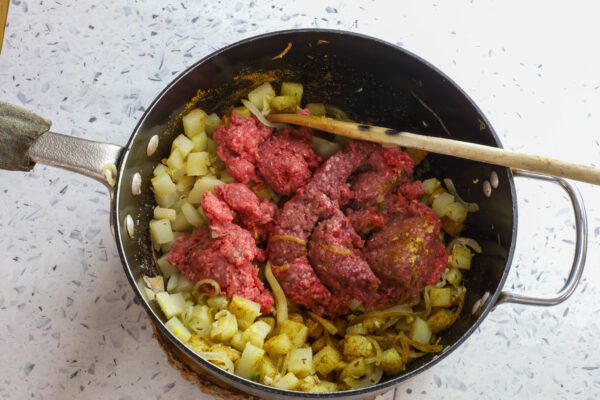 ground beef in pan with onions and potatoes.
