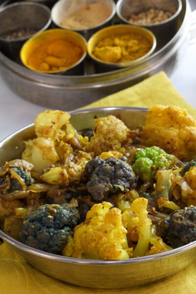 Curried cauliflower vertical shot with spices in the background.