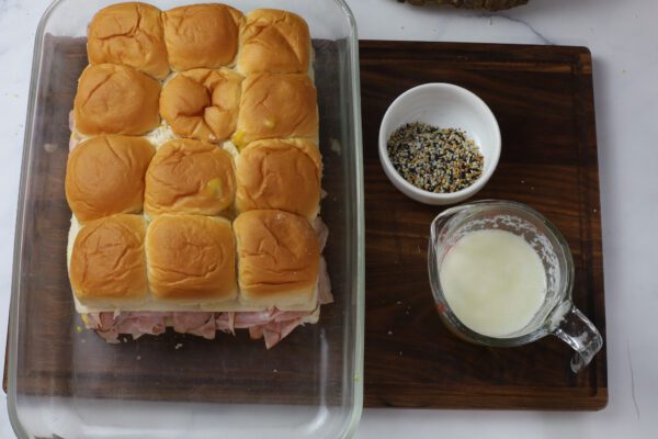 ham and cheese sliders on wooden board with butter in cup.